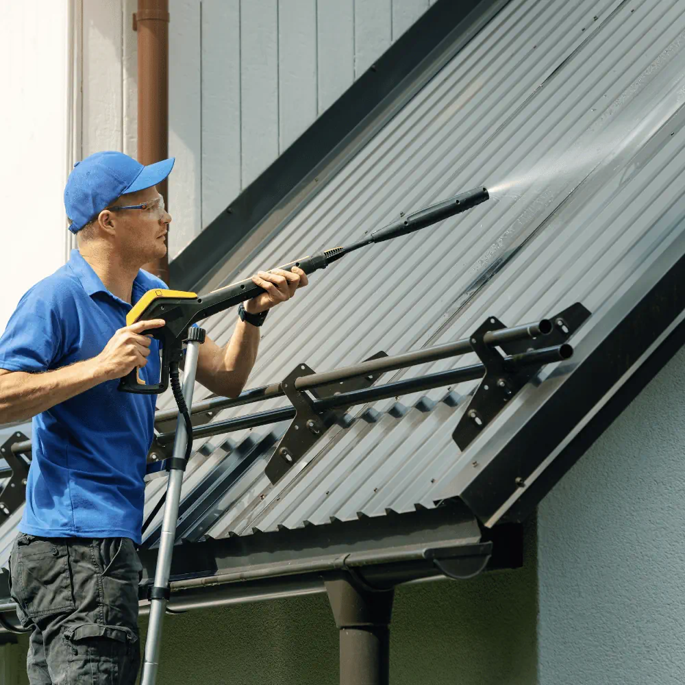 Technician pressure washing a metal roof exterior to remove dirt and buildup