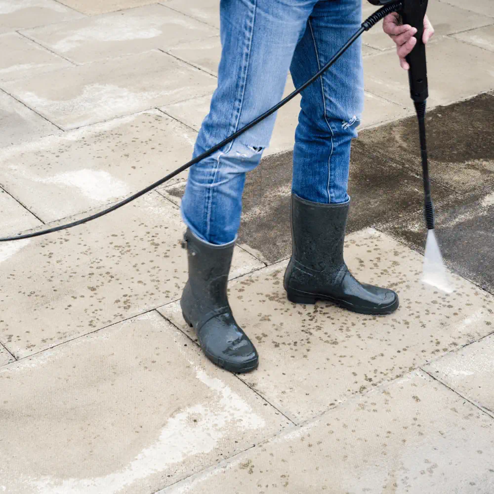 Person pressure washing patio paving slabs, removing dirt and grime outdoors