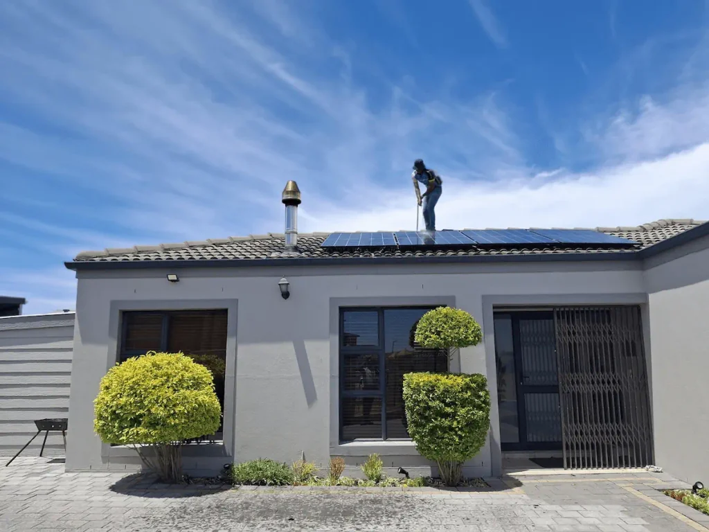Technician cleaning rooftop solar panels on a residential home using a safe low-pressure washing method